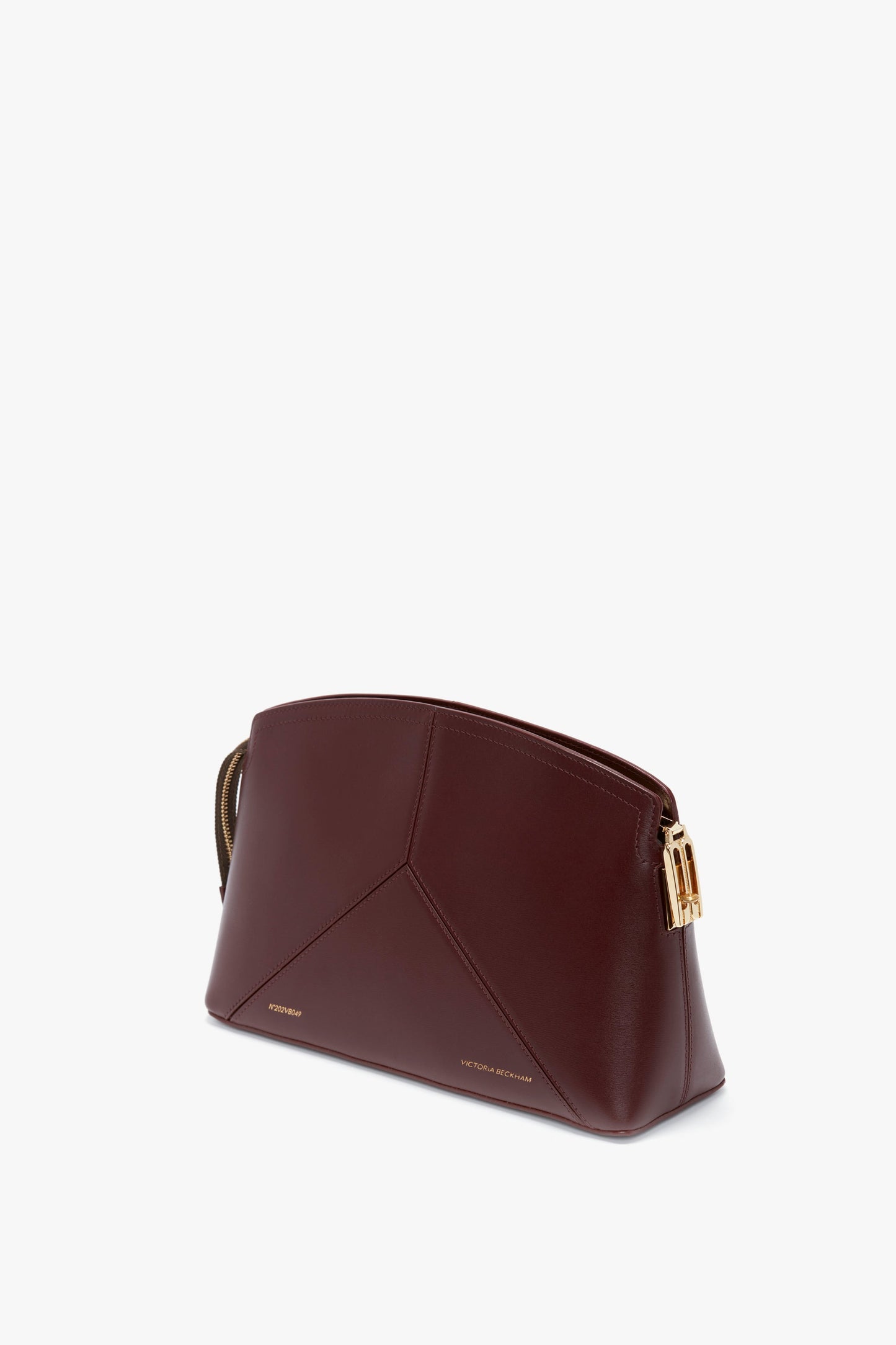 A triangular, burgundy leather Victoria Clutch Bag In Burgundy Leather featuring gold hardware detailing and minimalistic, embossed text branding à la Victoria Beckham.