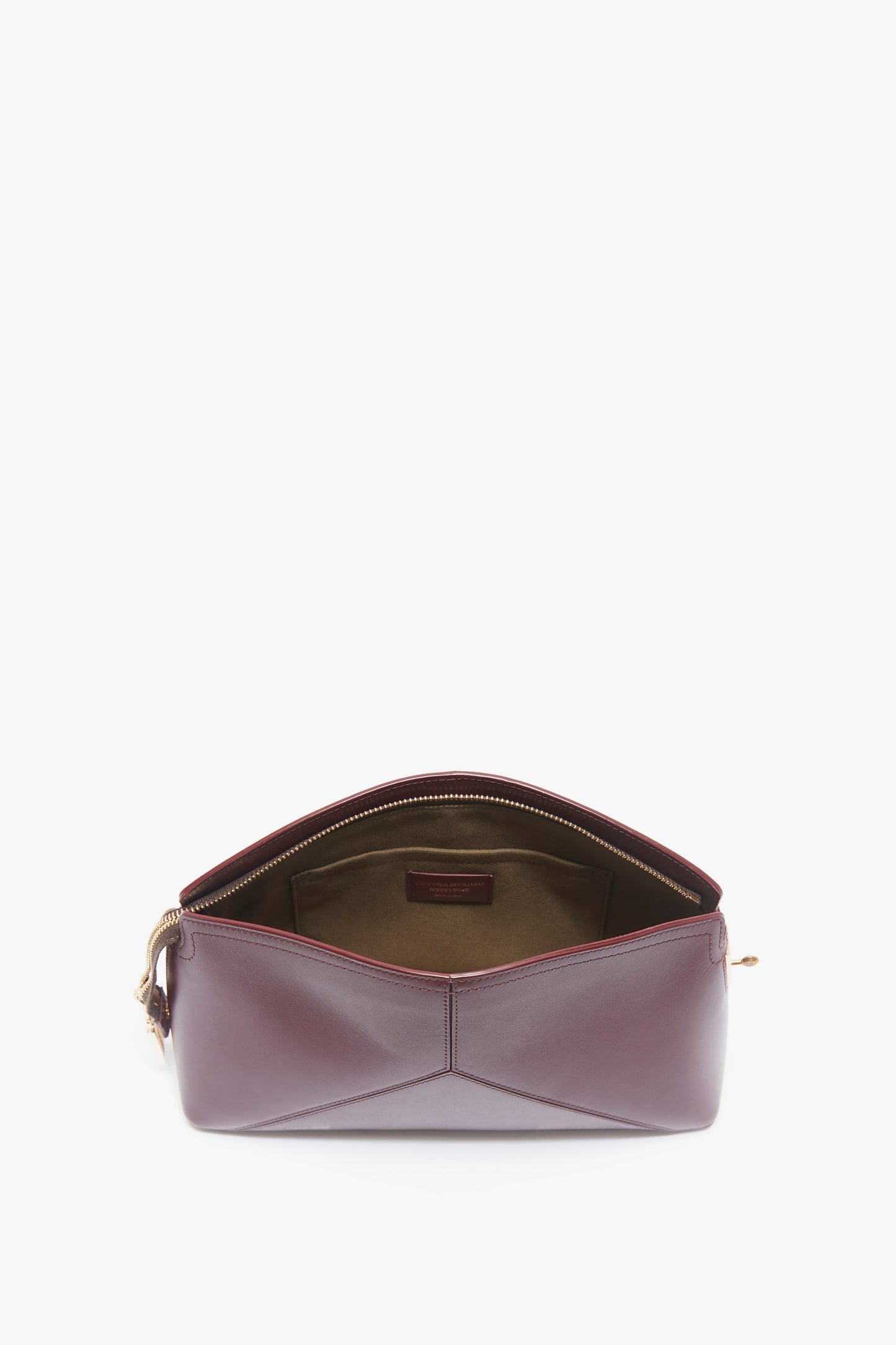 A Victoria Clutch Bag In Burgundy Leather by Victoria Beckham with a zip closure is open, revealing a beige interior lining and a small interior pocket, reminiscent of Victoria Beckham's iconic clutch bag designs.