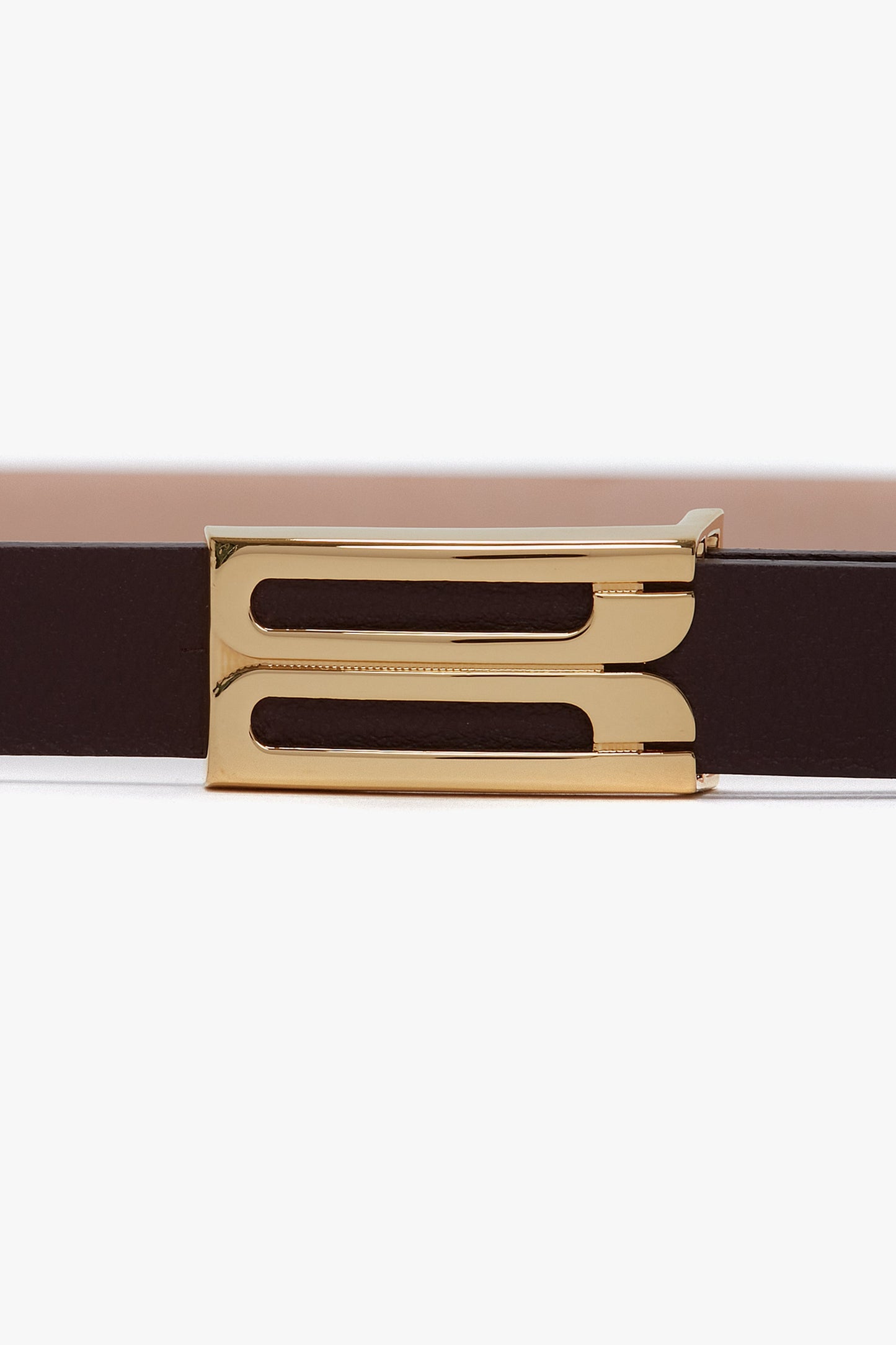A close-up view of the Victoria Beckham Frame Belt In Burgundy Leather with gold hardware, featuring a rectangular buckle with two parallel cut-out lines.