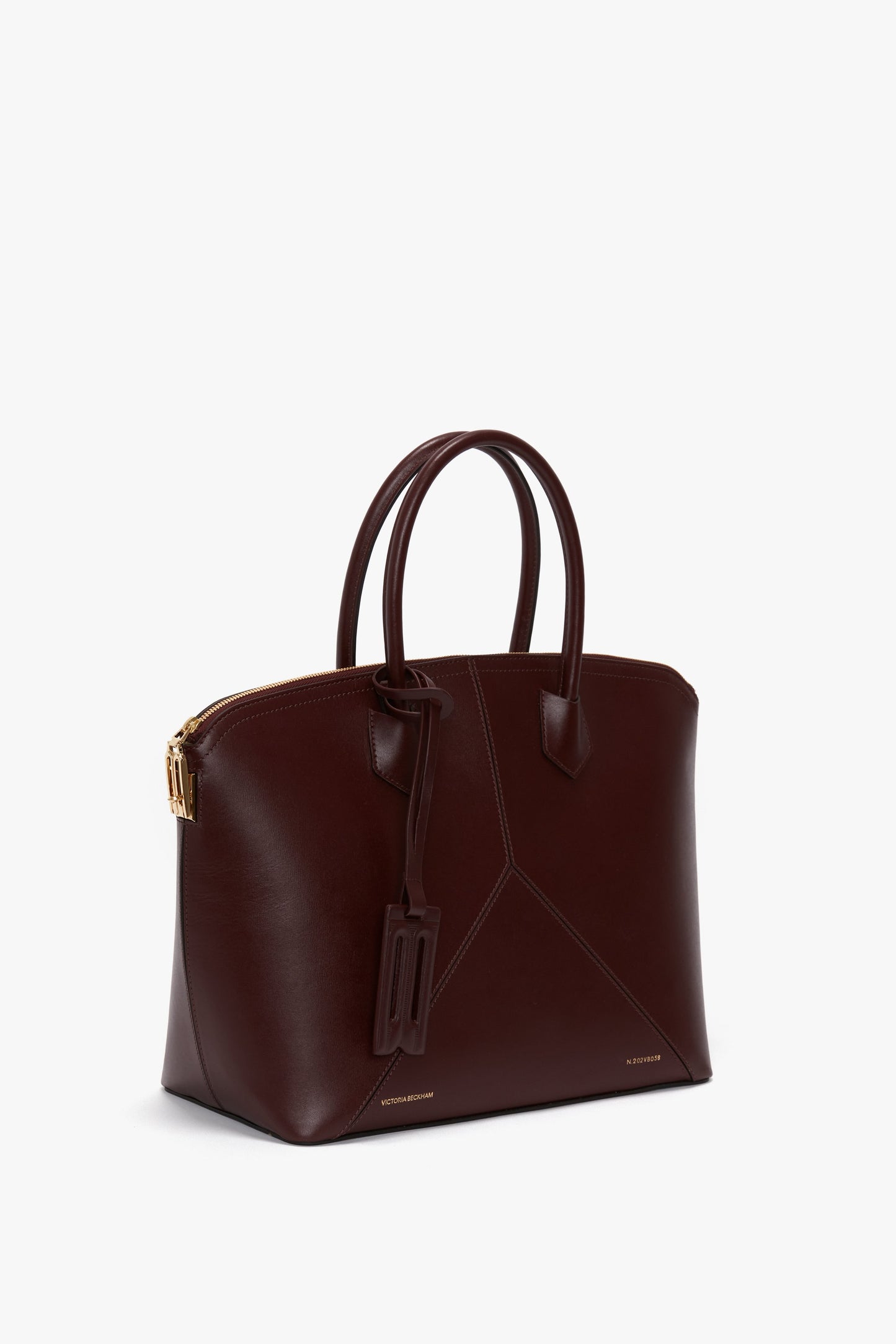 A burgundy leather Victoria Bag In Burgundy Leather by Victoria Beckham with two handles, gold hardware, a luggage tag, and an adjustable strap.