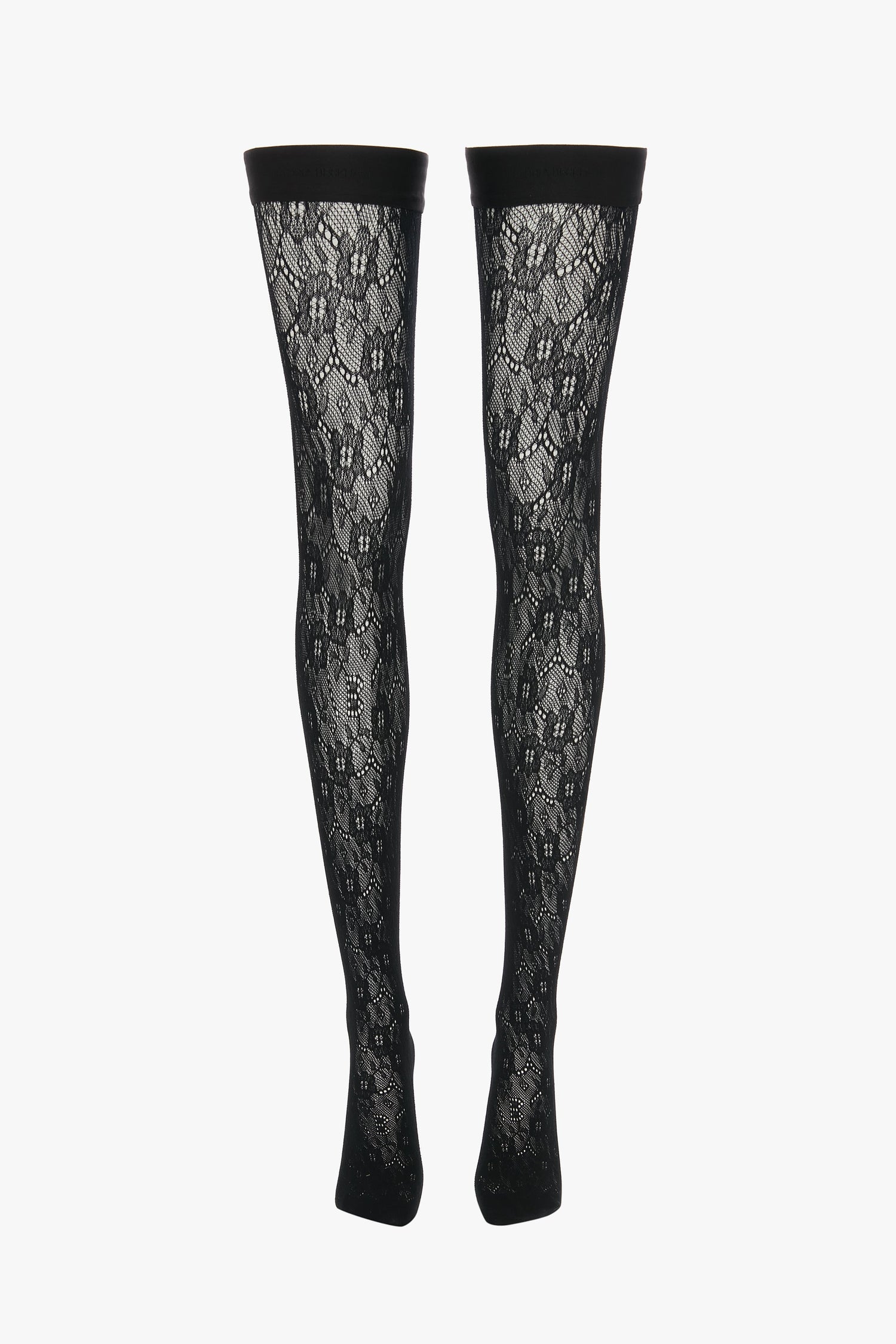 A pair of Exclusive VB Monogram Lace Hold-Ups In Black by Victoria Beckham, these black lace patterned thigh-high stockings feature a sheer finish and a solid black band at the top, displayed vertically.