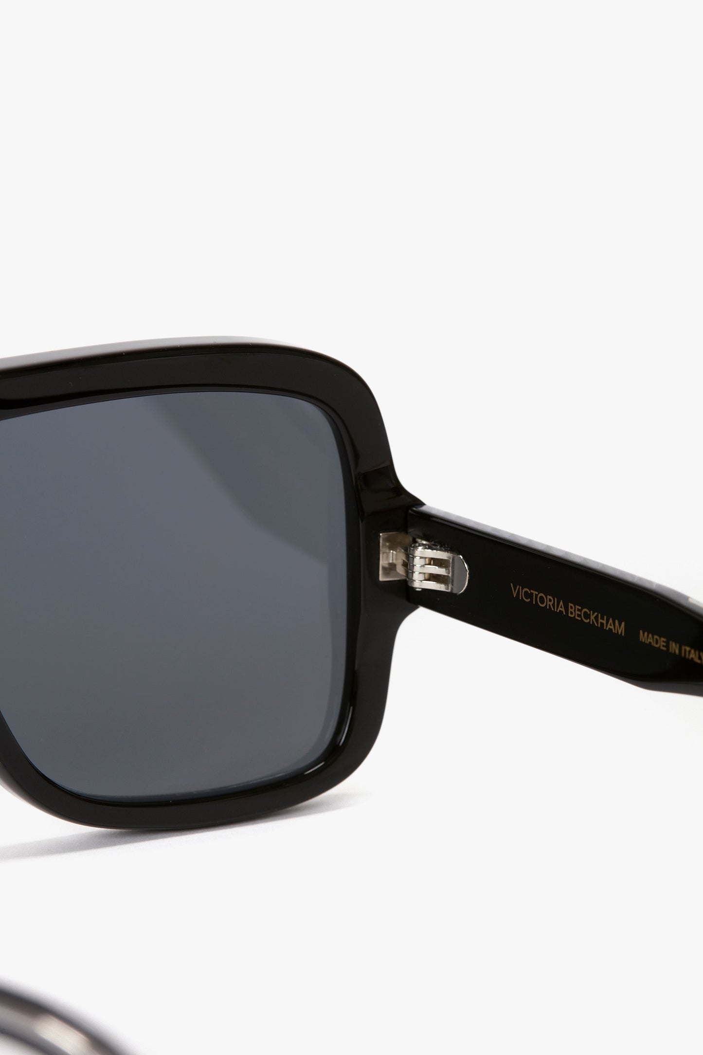Close-up of Layered Mask Sunglasses In Black-Silver-Mirror with dark lenses and rectangular shape. "Victoria Beckham" and "Made in Italy" are inscribed on the frame's arm, which features acetate temples.