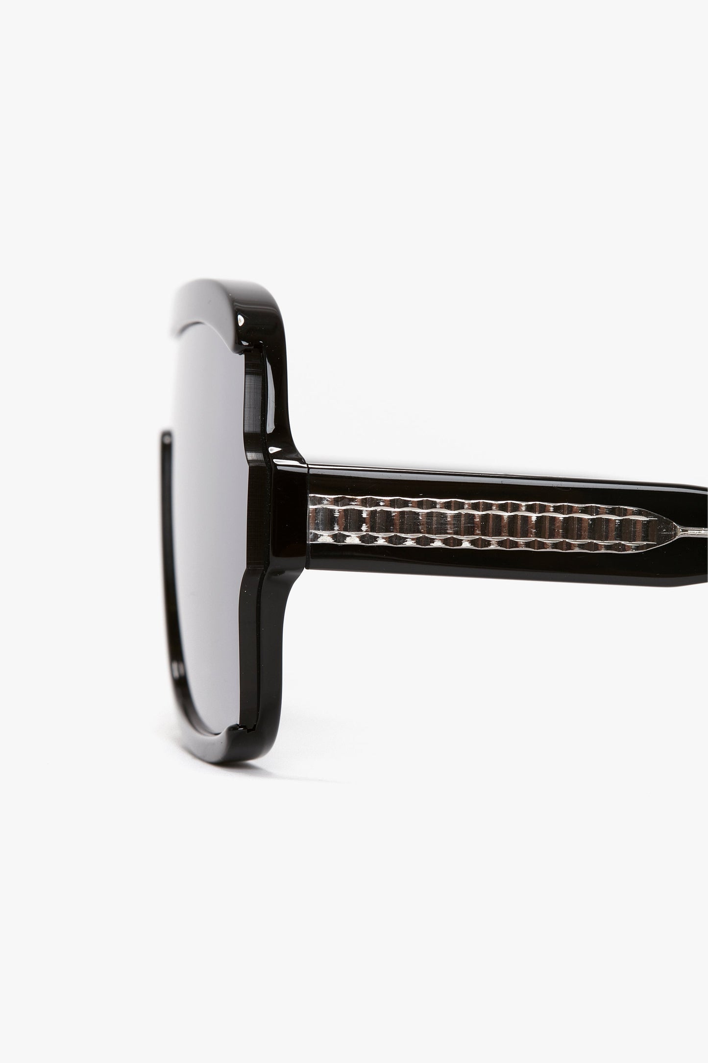 Close-up side view of a pair of Layered Mask Sunglasses In Black-Silver-Mirror by Victoria Beckham with a rectangular shape and tinted lenses, featuring acetate temples adorned with a guilloch pattern.