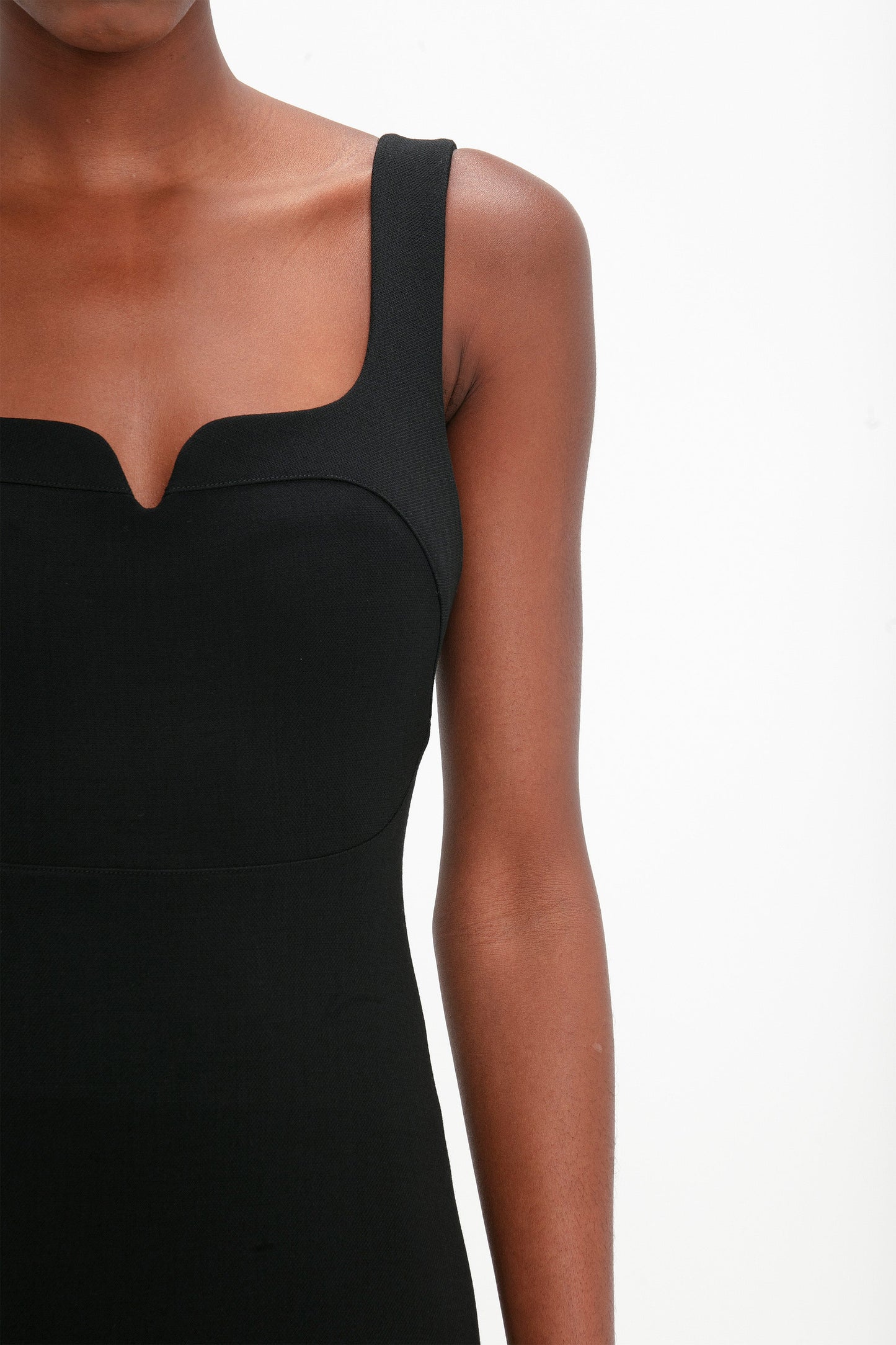 Person wearing a Victoria Beckham Sleeveless Fitted T-Shirt Dress In Black with a square neckline, shown from the shoulders to the waist against a plain white background.