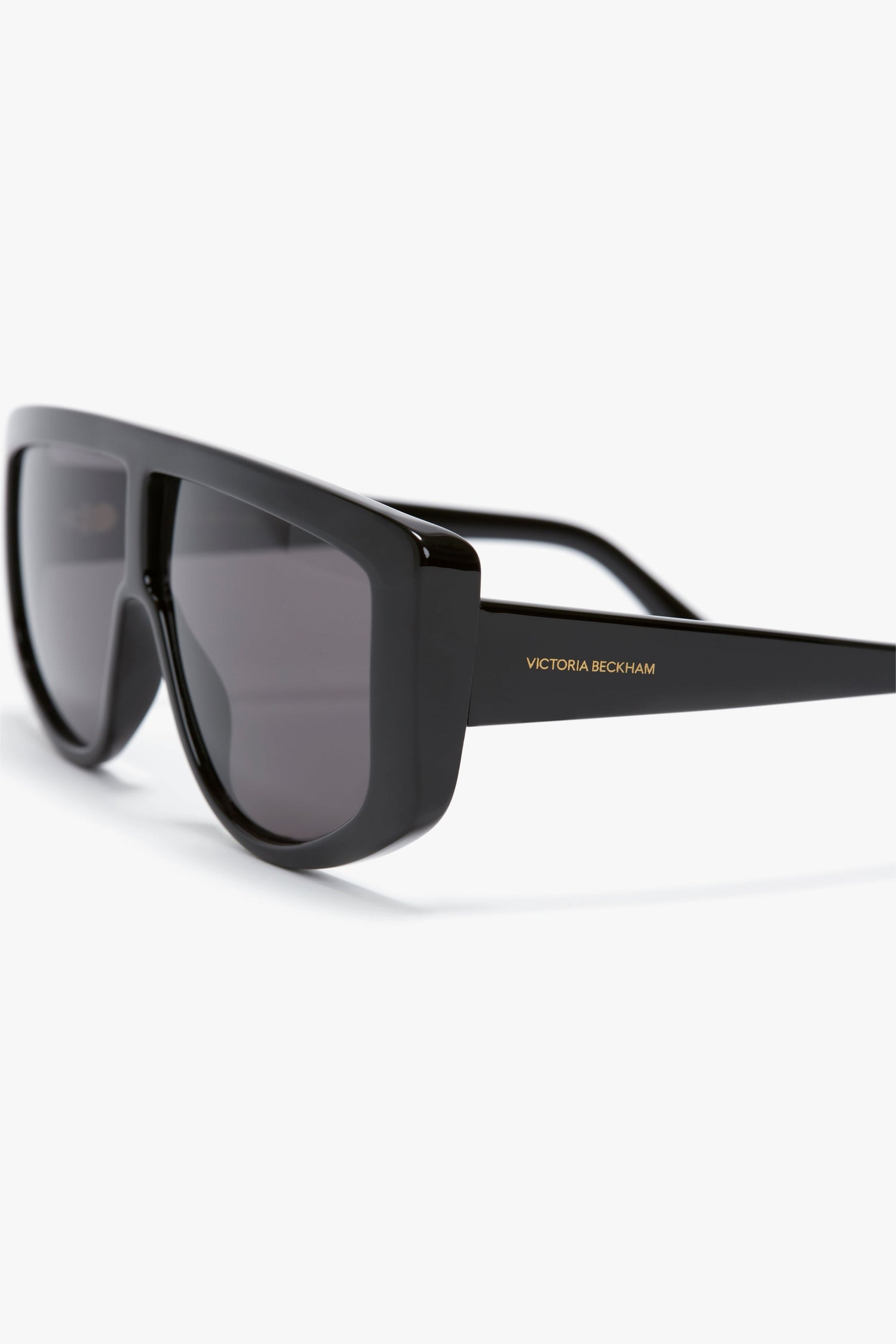 A pair of Acetate Visor Sunglasses In Black with black tonal lenses and the brand name "Victoria Beckham" written on the arm.