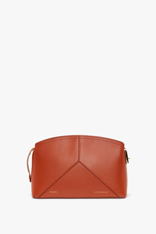 A Victoria Beckham Victoria Clutch Bag In Tan Leather with minimalistic design and subtle stitching, featuring a small handle on the side, a branded padlock, and a zip closure.