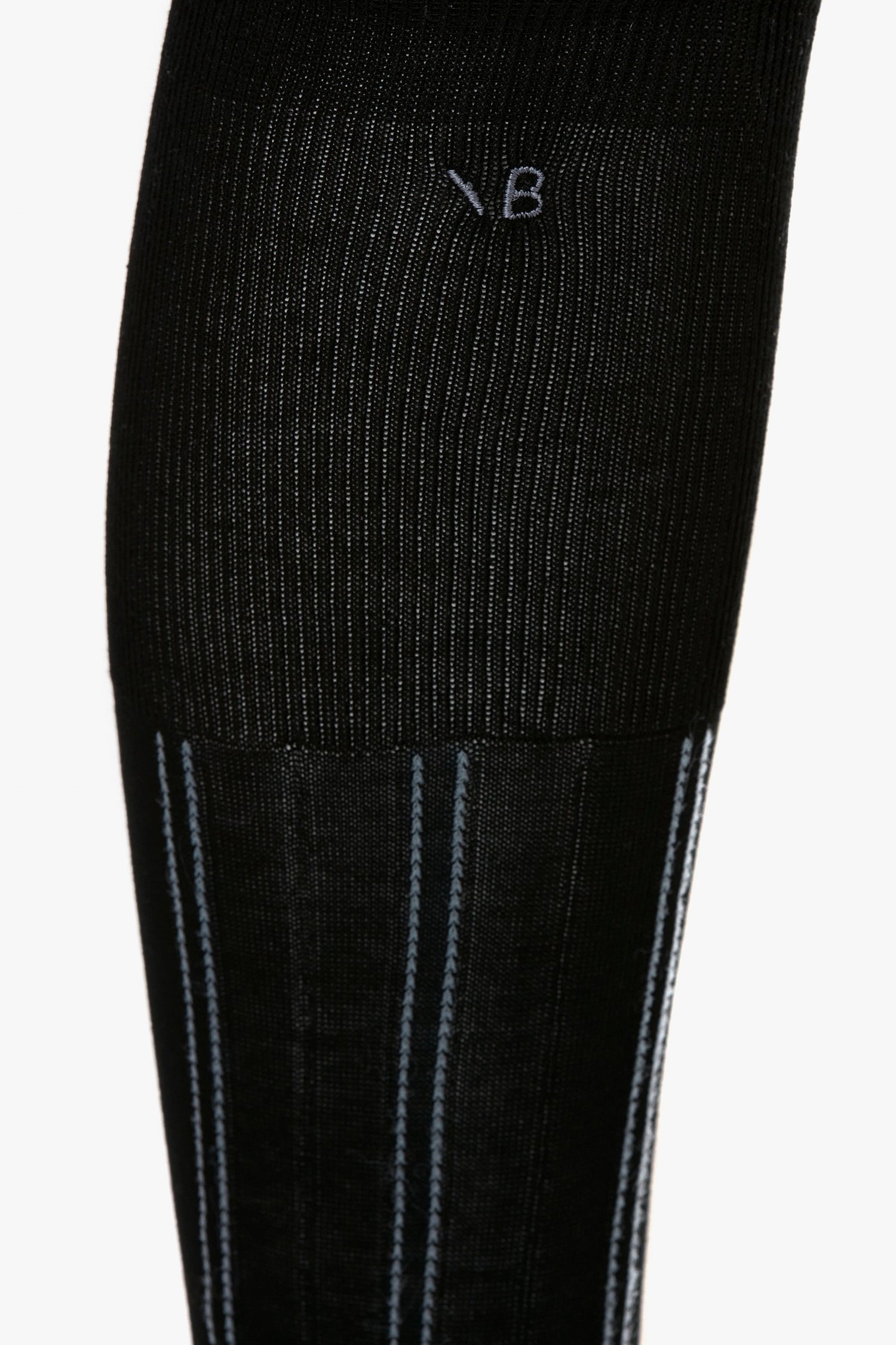 Close-up of a black ribbed sock with gray vertical stripes and the letters "V B" stitched on the upper part, showcasing its contemporary design. The Victoria Beckham Superfine Rib Socks In Black like these are a wardrobe essential for any modern closet.