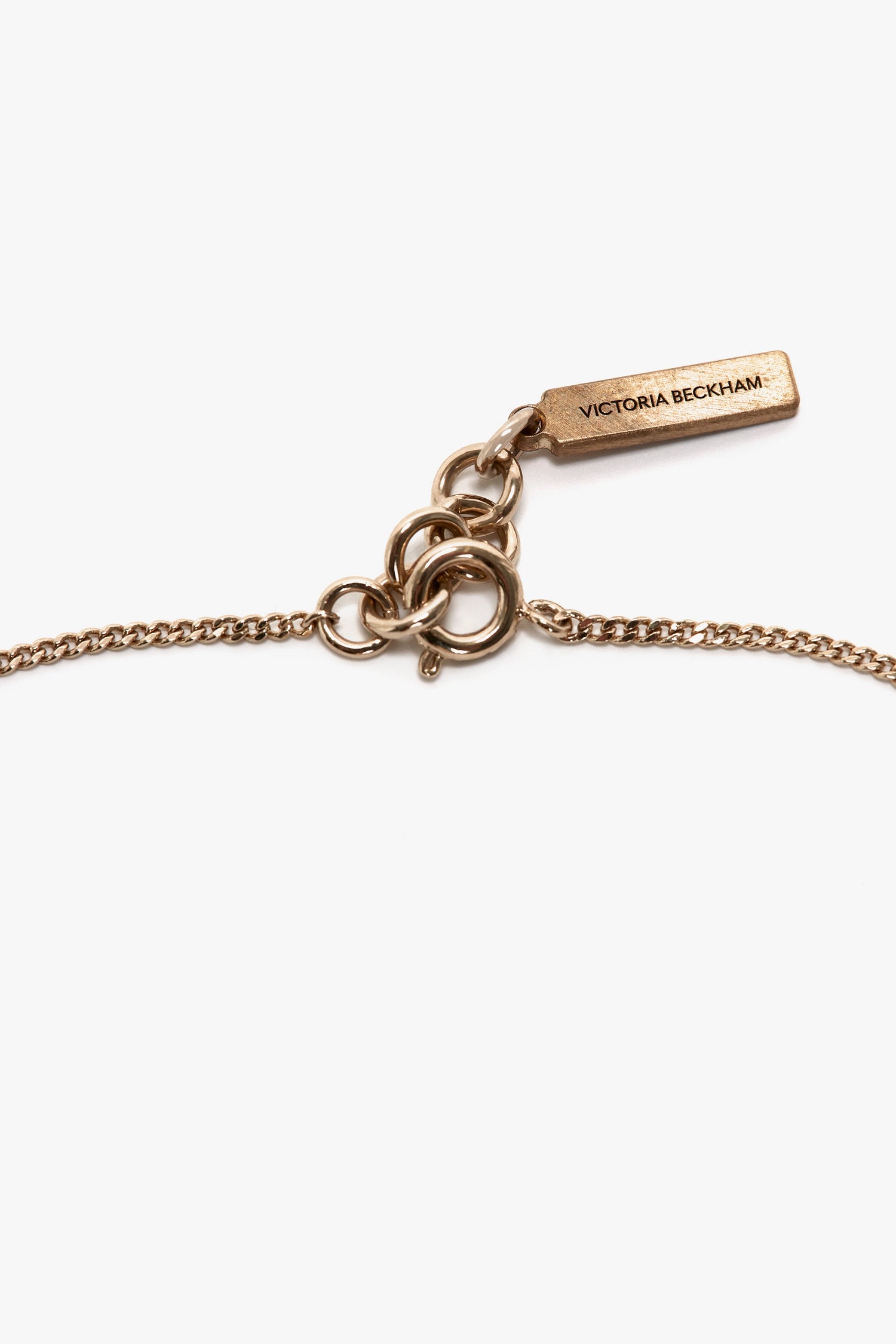 Close-up view of an Exclusive Camellia Flower Bracelet In Gold with circular links, an adjustable chain, and a rectangular tag engraved with "Victoria Beckham.