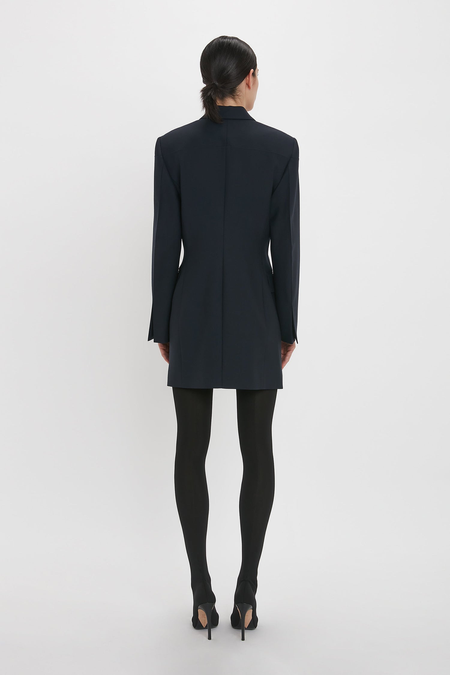 Person with long hair tied back, wearing the *Exclusive Fold Shoulder Detail Dress In Midnight* by *Victoria Beckham*, paired with black tights and high heels, standing with their back to the camera against a plain white background.