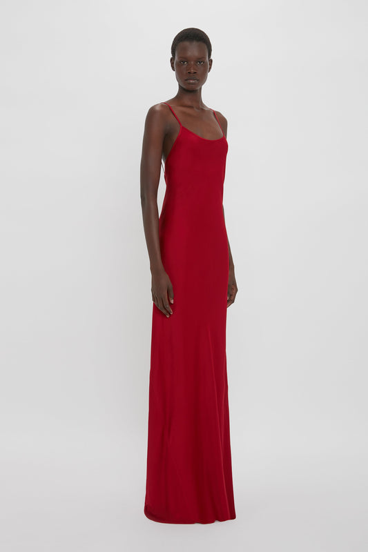 A person stands wearing a 1990s-inspired Victoria Beckham Low Back Cami Floor-Length Dress in Poppy Red, bias cut to perfection, against a plain white background.