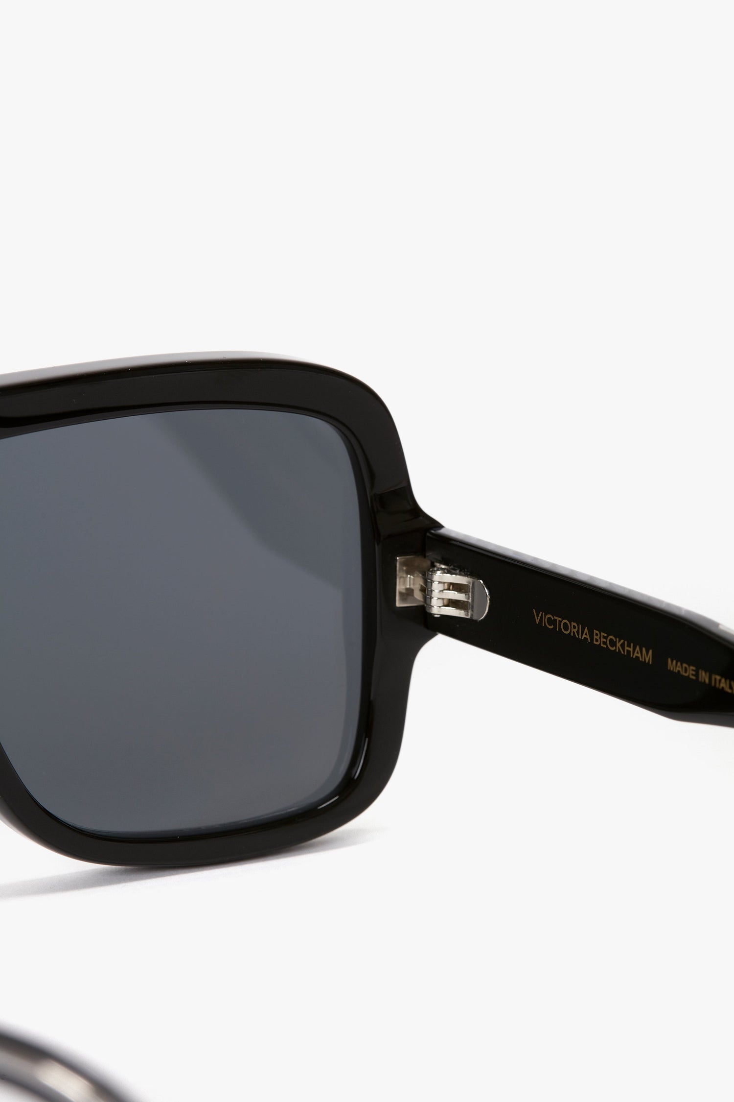 Close-up of Layered Mask Sunglasses In Black-Silver-Mirror with dark lenses and rectangular shape. "Victoria Beckham" and "Made in Italy" are inscribed on the frame's arm, which features acetate temples.