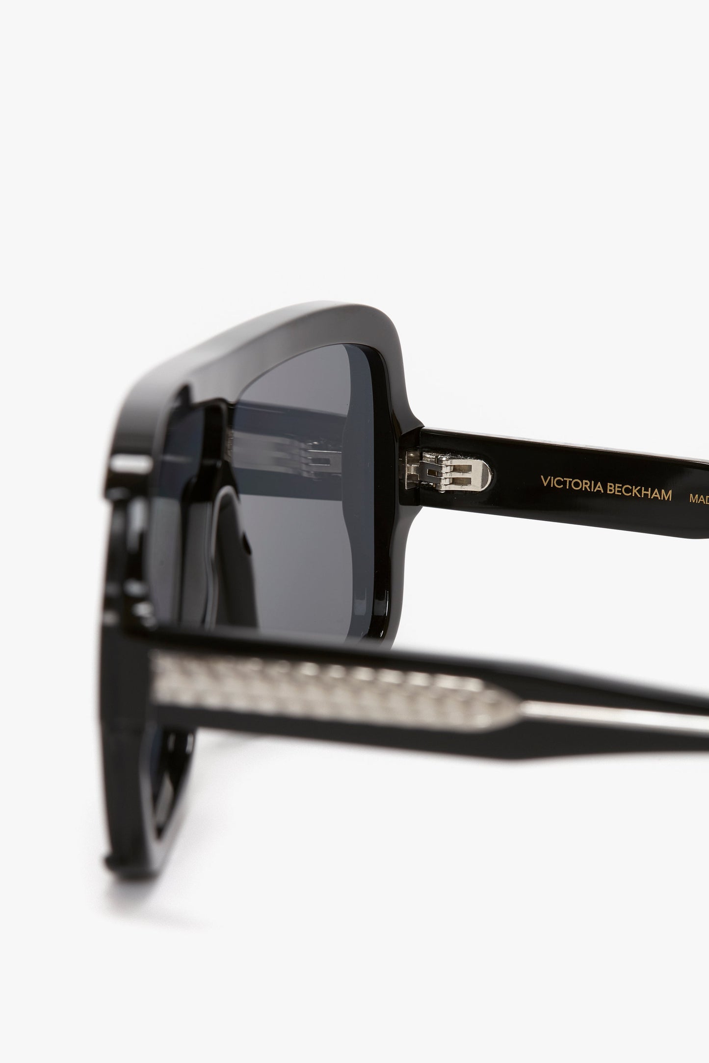 Close-up of black Victoria Beckham Layered Mask Sunglasses In Black-Silver-Mirror, showcasing the rectangular shape and acetate temples featuring the brand's logo and guilloch pattern design details.