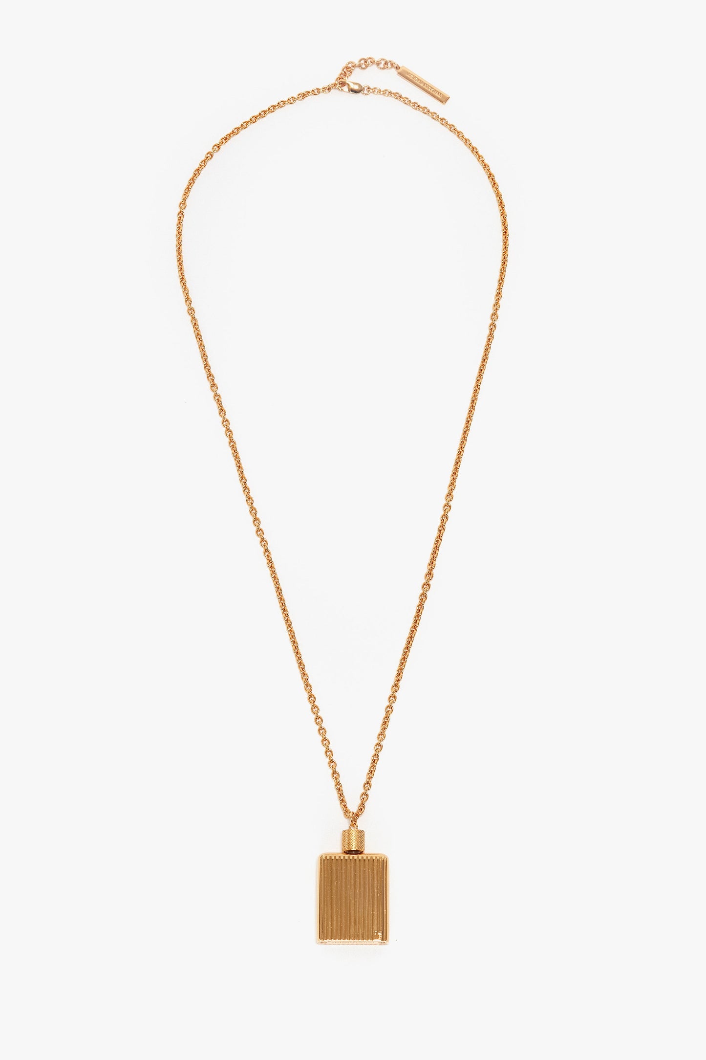 A gold necklace with a rectangular, gold brushed brass pendant featuring vertical grooves, reminiscent of the Victoria Beckham Exclusive Perfume Bottle Necklace In Brushed Gold.