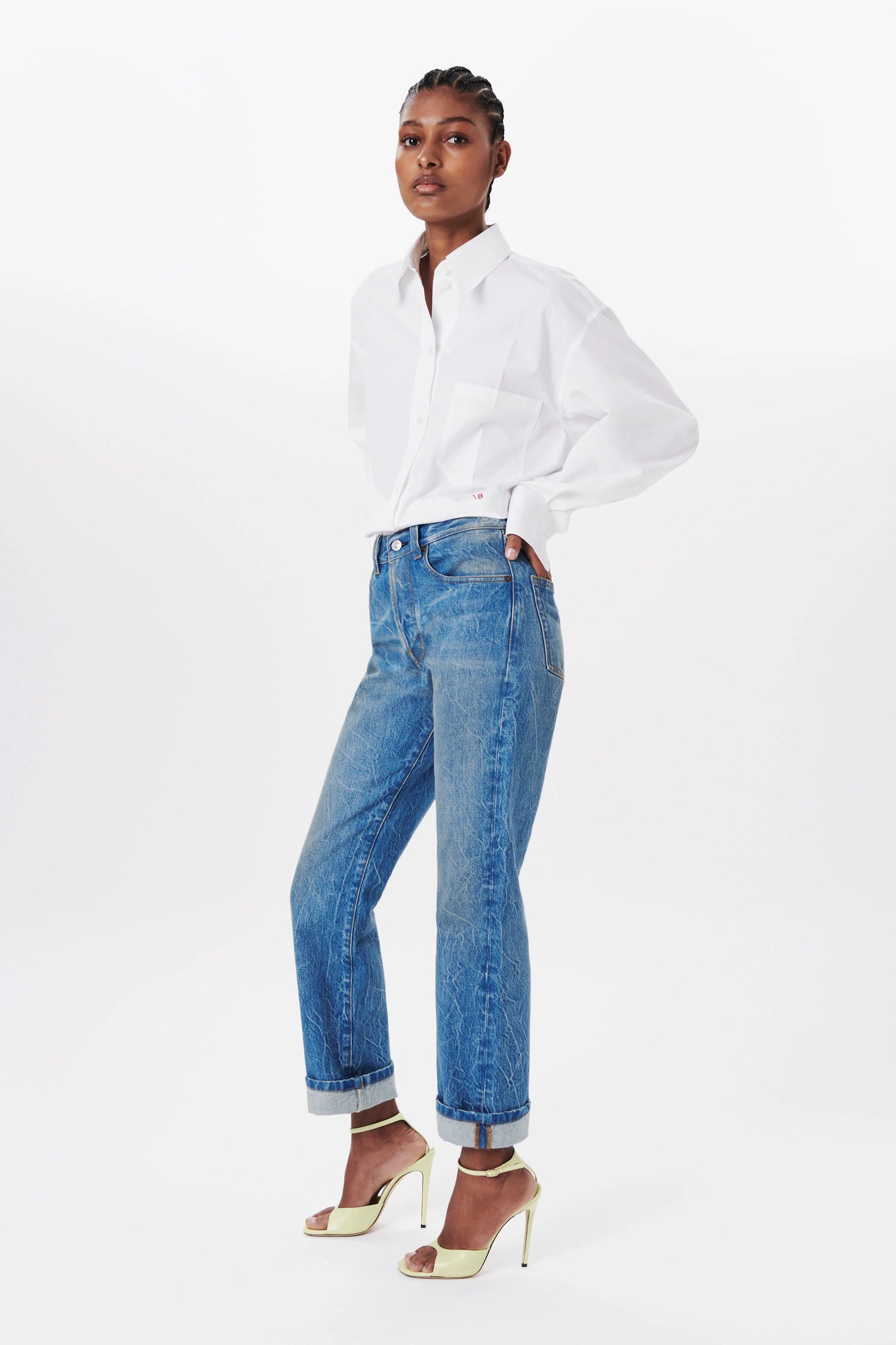 The model wears the Cropped Long Sleeve Shirt from Victoria Beckham. A designer shirt with a back box pleat and in a white colour, with VB’s monogram in front.